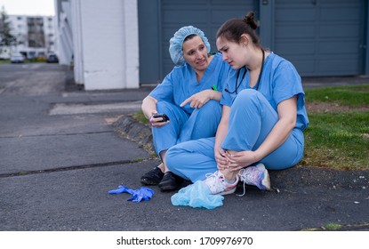 Two Sad Nurses In Scrubs Taking A Break Outside On A Spring Evening. Overworked Healthcare Workers Concept.