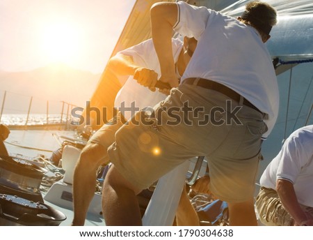 Two sailing crew members working rigging on sail boat with lens fare