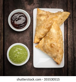 Two Samosas Served With Mint Coriander Chutney And Tamarind Chutney