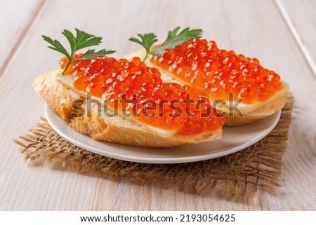 Two sandwiches with red caviar on a saucer over wooden table. Gourmet appetizer of trout caviar on a french baguette slice with butter. Salted salmon roe for fish delicacy concept. Front view.
