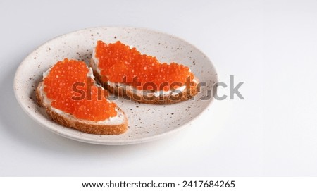 Two sandwiches with red caviar on a plate. A delicious appetizer of trout caviar on a slice of bread with cream cheese. Salted salmon caviar for fish delicacy concept.