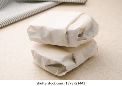 Two Sandwiches Wrapped In Parchment Paper On Kitchen Table