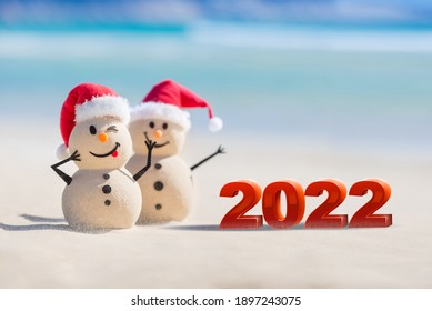 Two Sandy Christmas Snowmen are celebrating a Happy New Year on a beautiful beach with 2022 3d text, concept for new year 2022