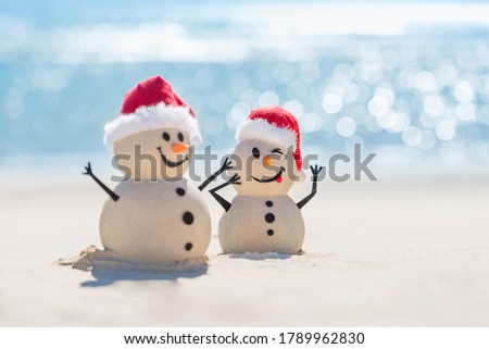 Two Sandy Christmas Snowmen are celebrating Christmas on a beautiful beach with beautiful bokeh in the background, one of them is only in focus