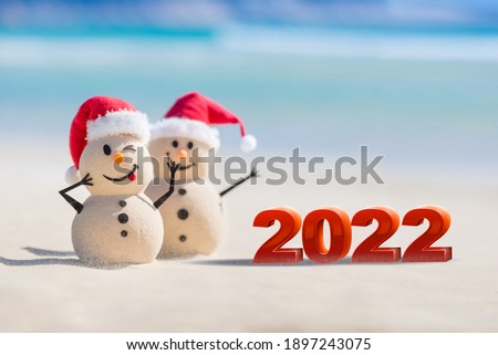 Two Sandy Christmas Snowmen are celebrating a Happy New Year on a beautiful beach with 2022 3d text, concept for new year 2022
