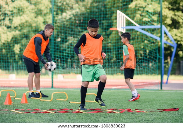 Two\
school boys are running ladder drills on the turf during football\
summer camp. Intense soccer training with\
coach.