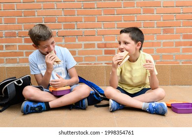 Two School Children Happily Eating A Sandwich During School Recess.