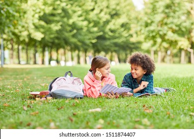 Two School Children Lying Together On Green Grass With Books And Talking To Each Other During Reading