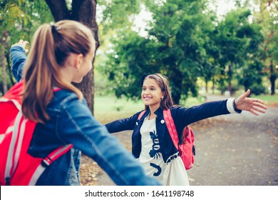 Two School Friends Hugging, Meet In The Park. Walking Into Each Other With Open Arms And Smiling. The Concept Of School, Study, Education, Friendship, Childhood