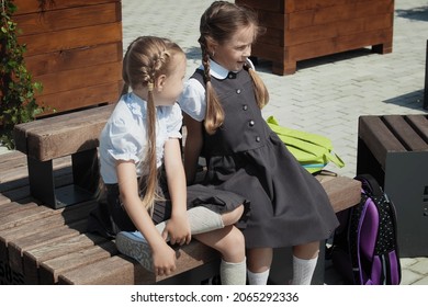 Two School Girls Talks At Schoolyard, Talking And Laughing During Recess Time In Elementary School. Schoolmates Playing At School Break Outdoors. Back To School Concept.