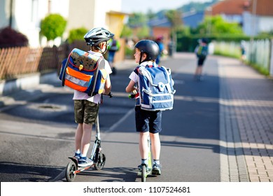 Two school kid boys in safety helmet riding with scooter in the city with backpack on sunny day. Happy children in colorful clothes biking on way to school. Safe way for kids outdoors to school. - Powered by Shutterstock