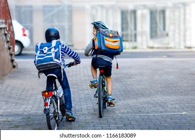 Two School Kid Boys In Safety Helmet Riding With Bike In The City With Backpacks. Happy Children In Colorful Clothes Biking On Bicycles On Way To School. Safe Way For Kids Outdoors To School