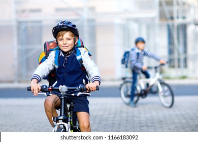 Two School Kid Boys In Safety Helmet Riding With Bike In The City With Backpacks. Happy Children In Colorful Clothes Biking On Bicycles On Way To School. Safe Way For Kids Outdoors To School