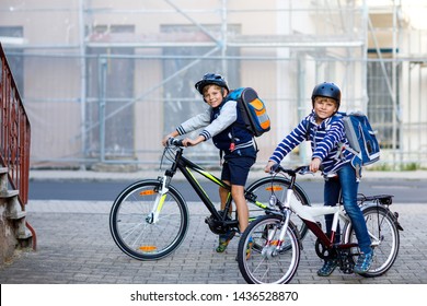 Two School Kid Boys In Safety Helmet Riding With Bike In The City With Backpacks. Happy Children In Colorful Clothes Biking On Bicycles On Way To School. Safe Way For Kids Outdoors To School