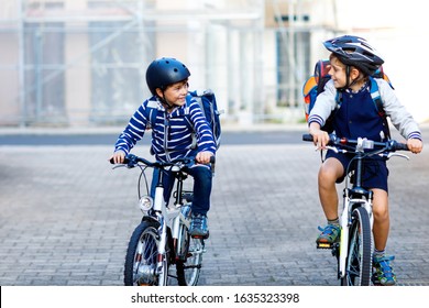 Two School Kid Boys In Safety Helmet Riding With Bike In The City With Backpacks. Happy Children In Colorful Clothes Biking On Bicycles On Way To School. Safe Way For Kids Outdoors To School