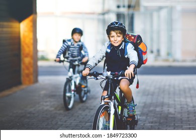 Two School Kid Boys In Safety Helmet Riding With Bike In The City With Backpacks. Happy Children In Colorful Clothes Biking On Bicycles On Way To School. Safe Way For Kids Outdoors To School