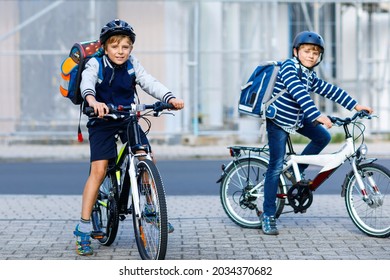 Two School Kid Boys In Safety Helmet Riding With Bike In The City With Backpacks. Happy Children In Colorful Clothes Biking On Bicycles On Way To School. Safe Way For Kids Outdoors To School