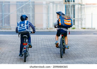 Two School Kid Boys In Safety Helmet Riding With Bike In The City With Backpacks. Happy Children In Colorful Clothes Biking On Bicycles On Way To School. Safe Way For Kids Outdoors To School