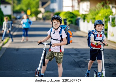 Two school kid boys in safety helmet riding with scooter in the city with backpack on sunny day. Happy children in colorful clothes biking on way to school. Safe way for kids outdoors to school - Powered by Shutterstock