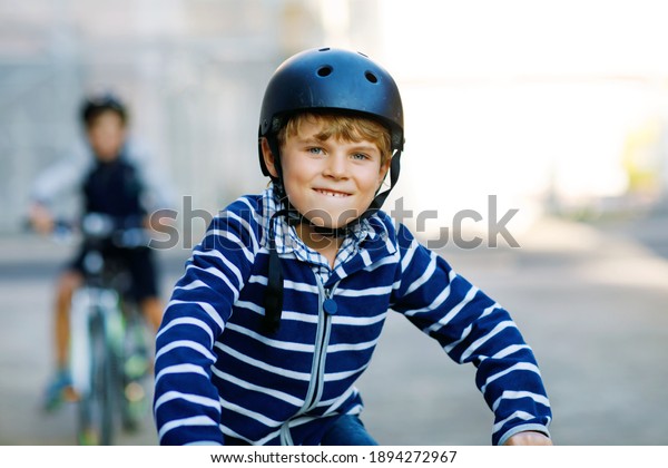 Two\
school kid boys in safety helmet riding with bike in the city with\
backpacks. Happy children in colorful clothes biking on bicycles on\
way to school. Safe way for kids outdoors to\
school