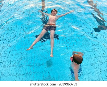 Two School Kids Boys Playing And Splashing In An Outdoor Swimming Pool On Warm Summer Day. Happy Healthy Children Enjoying Sunny Weather In City Public Pool. Kids Activity Outdoors With Water.