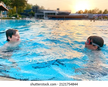 Two School Kids Boys Playing And Splashing In An Outdoor Swimming Pool On Warm Summer Day. Happy Healthy Children Enjoying Sunny Weather In City Public Pool. Kids Activity Outdoors With Water.