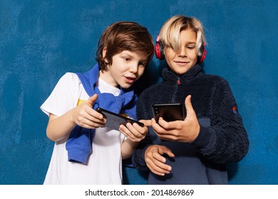 Two schoolboys playing online on smartphones devices together on blue background. New generation, kids and technology.