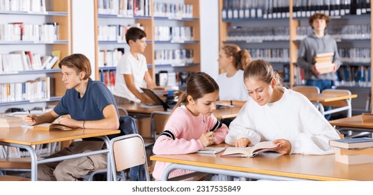 Two schoolgirls, preparing for lessons in the school library, take notes in a exercise book of the necessary material from ..the textbook, discussing topical issues - Powered by Shutterstock