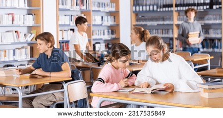Two schoolgirls, preparing for lessons in the school library, take notes in a exercise book of the necessary material from ..the textbook, discussing topical issues