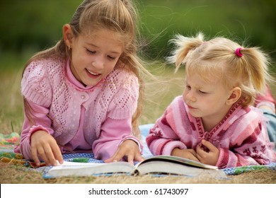  two schoolgirls is  reading  a big  book on the background of green meadows - Powered by Shutterstock