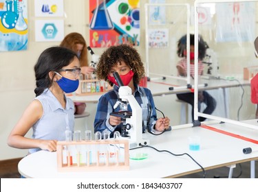 Two schoolgirls wearing face masks and looking at the microscope. Education back to school health safety during Covid19 Coronavirus pandemic. - Powered by Shutterstock