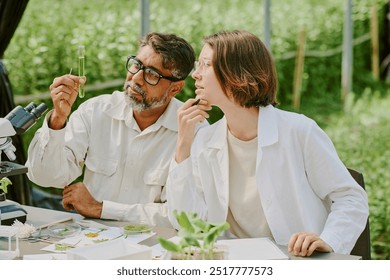 Two scientists analyzing plant samples outdoors, holding test tube and discussing results, surrounded by laboratory equipment and greenery under a shade structure - Powered by Shutterstock