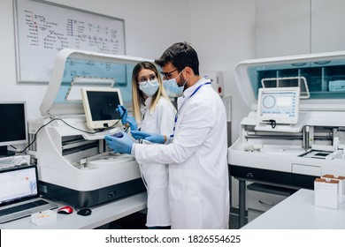 Two scientists or technicians with face protective masks work in laboratory on human blood samples.