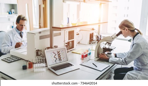 Two scientists are working in laboratory. Young female researcher and her senior supervisor are doing investigations on laboratory equipment.