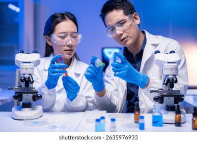 Two scientists are working on a project. One of them is holding a green bottle. The other one is holding a red bottle