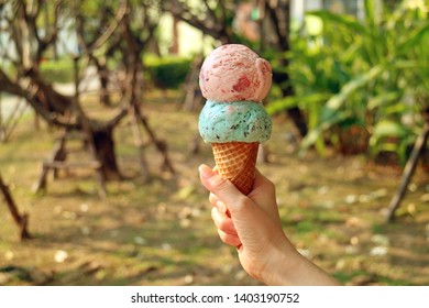 Two scoops of ice cream cone in woman's hand with blurry sunshine garden in background - Powered by Shutterstock