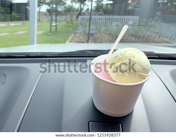 Two scoops of ice\
cream with durian and raspberry favor in white paper cups on front\
car consoles with space