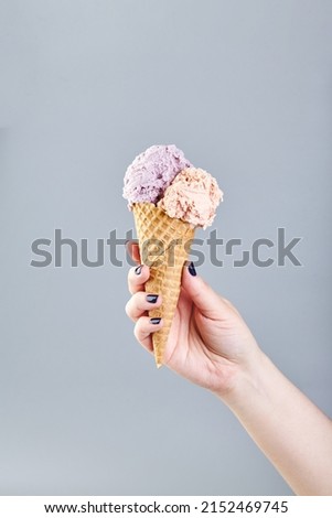 Two scoops of ice cream in waffle cone in female hand on gray background.