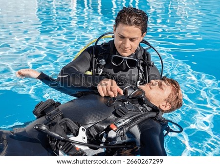 Two scuba divers practicing diver rescue skills in a pool, with one diver floating on his back and the other is unclipping his BCD