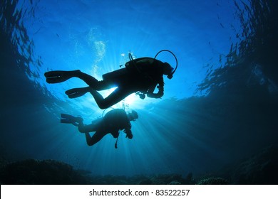 Two Scuba Divers, silhouettes against sunburst, in the ocean beside coral reef