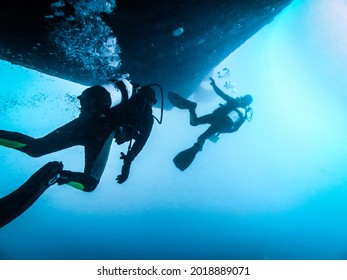 Two Scuba Divers Underwater Checking The Hull Of A Ship