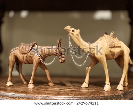 Two sculptures of a donkey and a camel, two wooden sculptures, stand opposite each other on a wooden shelf. They look at each other, each of them has a chain around their neck. High quality photo