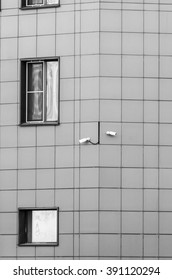 Two security cameras watching in different directions under the window of the building.