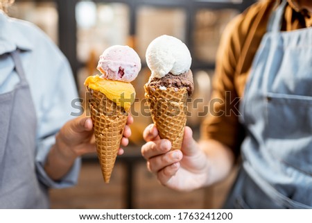 Two sellers cheering with yummy ice creams in waffle cone, having fun while selling ice cream at the shop, close-up