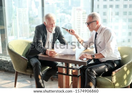 Two Senior businessman couple meeting in co working space and record voice or line call by smart mobile phone at skyscraper lounge