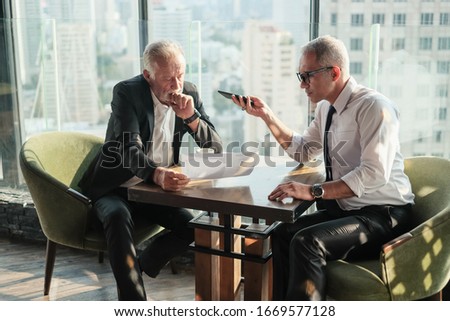 Two Senior businessman couple meeting in co working space and record voice or line call by smart mobile phone at skyscraper lounge