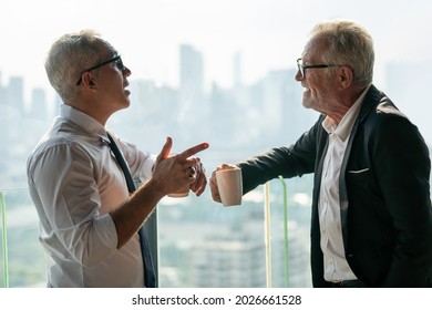 Two Senior Businessman Take A Break Drinking Coffee And Discussing Business Strategy In Coffee Shop At Modern Restaurant On A Tall Building Cityscape Background . Old Friend Talking Or Life Advice 