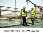 Two senior construction managers are standing on the bridge while talking and smiling