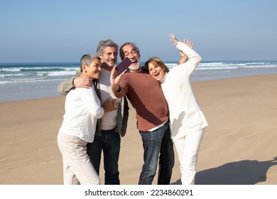 Two senior couples having fun at the beach, standing against sea background and taking selfie. Excited bearded man holding smartphone and making shot. Modern technology, friendship, leisure concept - Powered by Shutterstock