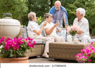 Two Senior Couples Having A Social Gathering Outside On A Patio In The Garden On Summer Afternoon. Making A Toast.